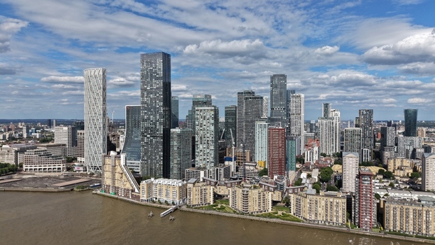 London United Kingdom 16 June 2026 Aerial view of the Canary Wharf skyline featuring modern skyscrapers and residential buildings along the River Thames under a blue sky.