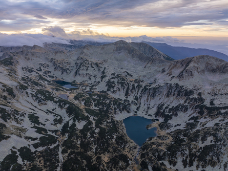 Aerial view of Pirin National Park with its dramatic rocky peaks glacial lakes and rugged terrain under a soft sunset sky in Blagoevgrad Province Bulgaria. Aerial view of Pirin National Park with its dramatic rocky peaks glacial lakes and rugged terrain under a soft sunset sky in Blagoevgrad Province Bulgaria.