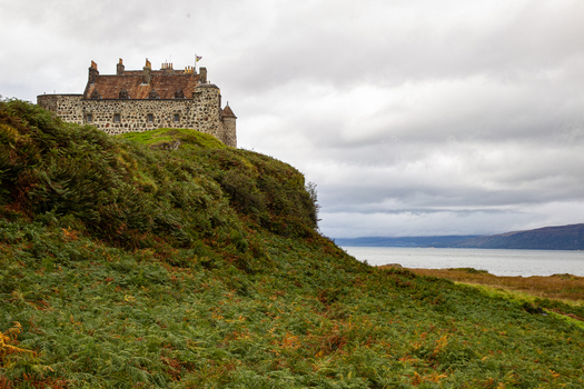 View of Duart Castle standing on a rocky cliff covered in green ferns overlooking the sea under a cloudy sky in Isle of Mull Scotland United Kingdom.