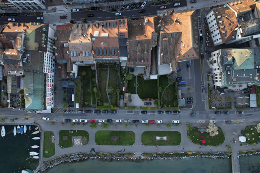 Aerial view of historic buildings with red tiled roofs lush private gardens and people walking along the lakeside promenade Morges Vaud Switzerland. Aerial view of historic buildings with red tiled roofs lush private gardens and people walking along the lakeside promenade Morges Vaud Switzerland.