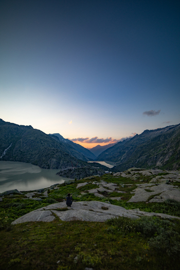 View of a person sitting on a rocky outcrop overlooking a mountain lake in the Swiss Alps at sunset in Airolo Ticino Switzerland. View of a person sitting on a rocky outcrop overlooking a mountain lake in the Swiss Alps at sunset in Airolo Ticino Switzerland.
