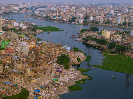 Aerial view of the Buriganga River flowing through densely packed urban buildings with small boats and green aquatic plants Keraniganj Dhaka Division Bangladesh. Aerial view of the Buriganga River flowing through densely packed urban buildings with small boats and green aquatic plants Keraniganj Dhaka Division Bangladesh.