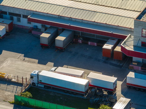 Aerial view of a logistics warehouse facility with multiple semi trucks and trailers parked at loading docks in Ancona Marche Italy. Aerial view of a logistics warehouse facility with multiple semi trucks and trailers parked at loading docks in Ancona Marche Italy.