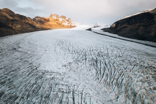Aerial view of the vast Skaftafell glacier tongue with deep crevasses and rugged mountain peaks under a soft sky Skaftafell Sveitarfelagid Hornafjordur Iceland. Aerial view of the vast Skaftafell glacier tongue with deep crevasses and rugged mountain peaks under a soft sky Skaftafell Sveitarfelagid Hornafjordur Iceland.