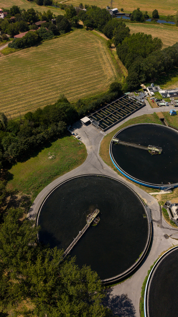 Aerial view of wastewater treatment plant with large circular sedimentation tanks surrounded by green fields and trees in Milan Lombardy Italy. Aerial view of wastewater treatment plant with large circular sedimentation tanks surrounded by green fields and trees in Milan Lombardy Italy.