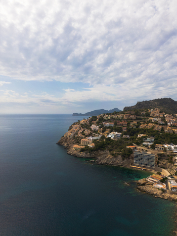 Aerial view of Port d Andratx with houses perched on rocky cliffs overlooking the Mediterranean Sea under a cloudy sky Port d Andratx Balearic Islands Spain. Aerial view of Port d Andratx with houses perched on rocky cliffs overlooking the Mediterranean Sea under a cloudy sky Port d Andratx Balearic Islands Spain.