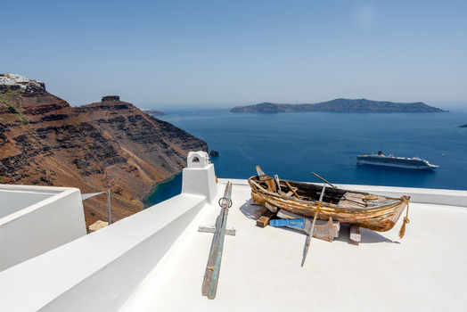 View of an old wooden boat resting on a white rooftop overlooking the caldera and the Aegean Sea in Fira Greece. View of an old wooden boat resting on a white rooftop overlooking the caldera and the Aegean Sea in Fira Greece.
