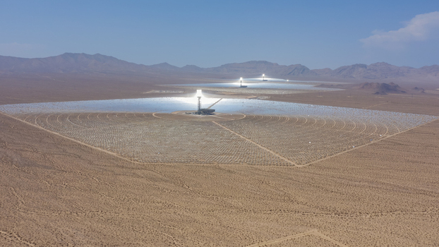 Aerial view of a large concentrated solar power plant with thousands of heliostat mirrors reflecting sunlight toward central solar towers in a vast desert landscape United States.