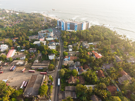 Aerial view of the coastal town with a main road lush palm trees residential houses and a modern hotel building by the ocean Galle Southern Province Sri Lanka.