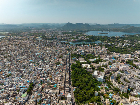 Aerial view of the historic city of Udaipur with its dense urban layout lush green areas and the expansive Lake Pichola in the background Udaipur Rajasthan India.