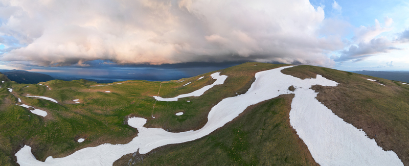 Aerial view of Le Colomby de Gex featuring snow patches on green mountain slopes under dramatic storm clouds in Echenevex Auvergne Rhone Alpes France. Aerial view of Le Colomby de Gex featuring snow patches on green mountain slopes under dramatic storm clouds in Echenevex Auvergne Rhone Alpes France.