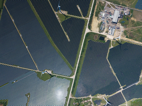 Aerial view of Chelveston Wind Farm featuring vast rows of solar panels and tall wind turbines under bright sunlight Wellingborough England United Kingdom. Aerial view of Chelveston Wind Farm featuring vast rows of solar panels and tall wind turbines under bright sunlight Wellingborough England United Kingdom.
