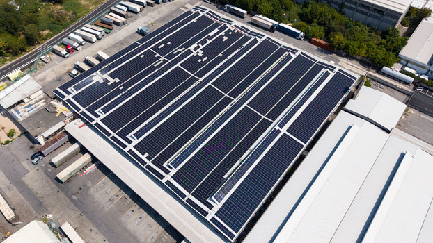 Aerial view of a logistics warehouse facility with extensive rooftop solar panels loading docks with semi trucks and surrounding industrial infrastructure in Melegnano Lombardy Italy.