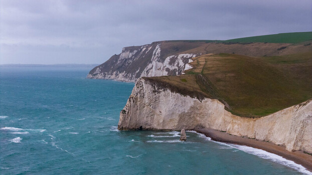 Aerial view of Durdle Door limestone arch on the Jurassic Coast with dramatic white chalk cliffs turquoise sea and grassy hills in Wareham England United Kingdom. Aerial view of Durdle Door limestone arch on the Jurassic Coast with dramatic white chalk cliffs turquoise sea and grassy hills in Wareham England United Kingdom.