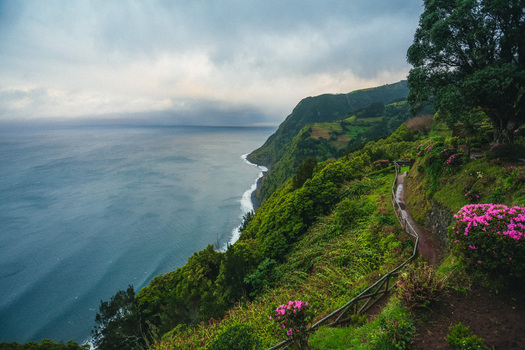 Aerial view of the rugged coastline where emerald cliffs meet the deep blue sea under a cloudy sky Nordeste Azores Portugal.