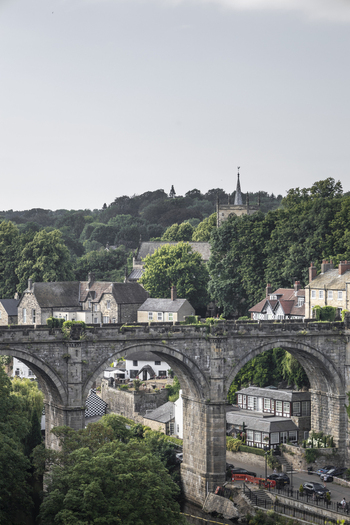 View of the historic Knaresborough Viaduct spanning the Nidd Gorge with lush green trees and a church spire in the background in Knaresborough England United Kingdom.