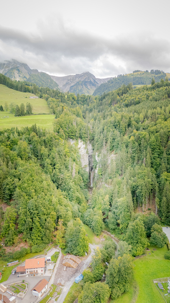 Aerial view of Grandvillard Waterfall cascading through a dense green forest with alpine mountains and a cloudy sky Grandvillard Fribourg Switzerland.