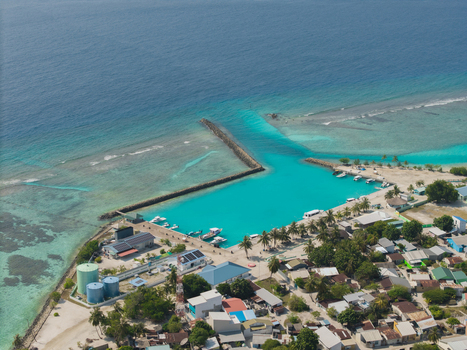 Aerial view of the turquoise lagoon meeting the deep blue sea contrasting with the buildings and lush greenery of the island Vashafaru Island Thiladhummathi Atoll Maldives.