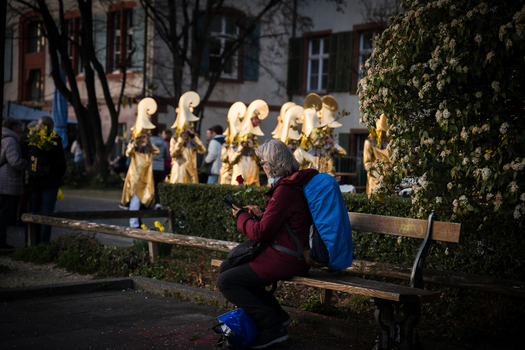 Basel Switzerland 10 March 2025 View of a woman on a bench amidst the vibrant Fasnacht festival where golden costumes gleam against the stark trees. Basel Switzerland 10 March 2025 View of a woman on a bench amidst the vibrant Fasnacht festival where golden costumes gleam against the stark trees.