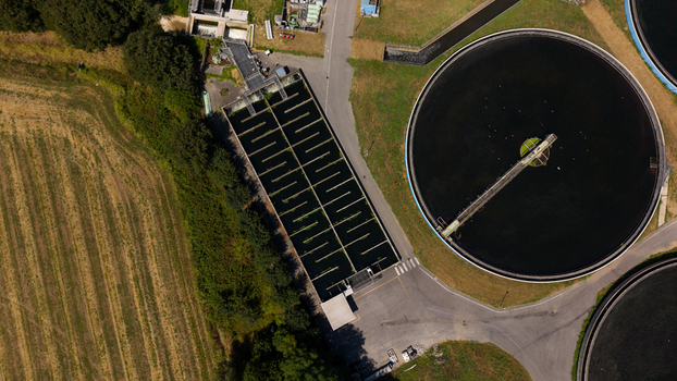 Aerial view of a wastewater treatment plant with circular sedimentation tanks and rectangular aeration basins surrounded by green fields in Milan Lombardy Italy. Aerial view of a wastewater treatment plant with circular sedimentation tanks and rectangular aeration basins surrounded by green fields in Milan Lombardy Italy.