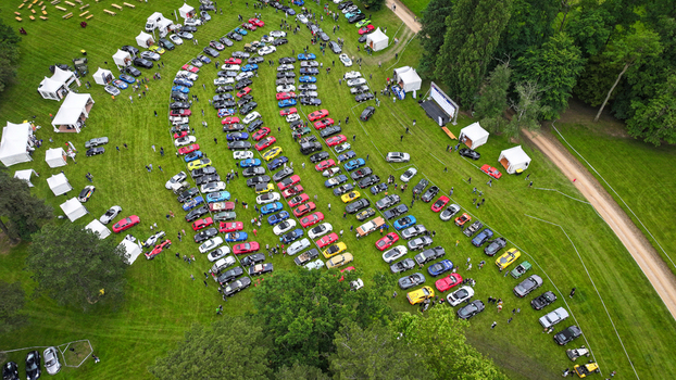 La Chapelle de Guinchay France 01 June 2024 Aerial view of rows of colorful sports cars parked on a green lawn during an outdoor automotive event with white tents.