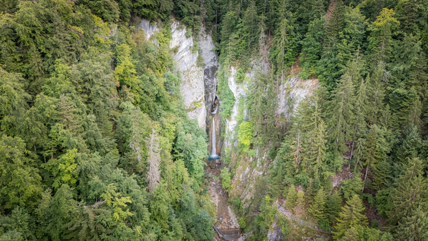 Aerial view of Grandvillard Waterfall cascading down a rocky cliff surrounded by lush green forest in Grandvillard Fribourg Switzerland.