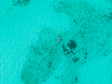 Aerial view of a small boat floating on the turquoise waters contrasting with the darker coral reefs beneath the surface Vashafaru Island Maldives.