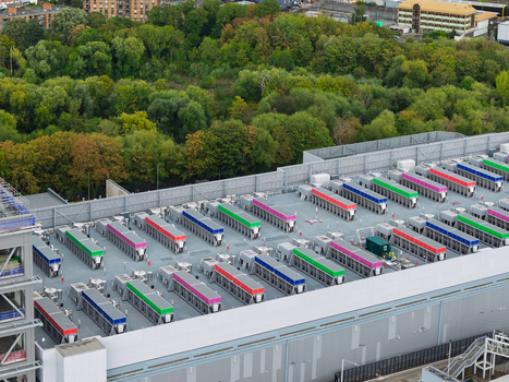 Aerial view of a data center roof featuring rows of colorful industrial cooling units surrounded by lush green trees in the United Kingdom.