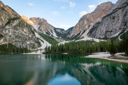 View of the Dolomites reflecting in the calm turquoise waters of a mountain lake surrounded by dense pine forests and rocky peaks in Rocca Pietore Veneto Italy. View of the Dolomites reflecting in the calm turquoise waters of a mountain lake surrounded by dense pine forests and rocky peaks in Rocca Pietore Veneto Italy.
