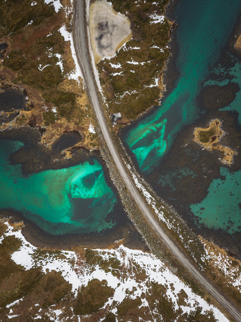 Aerial view of a road cutting through the vibrant turquoise waters and the rugged winter landscape of Flakstadbruene Flakstadbruene Nordland Norway. Aerial view of a road cutting through the vibrant turquoise waters and the rugged winter landscape of Flakstadbruene Flakstadbruene Nordland Norway.