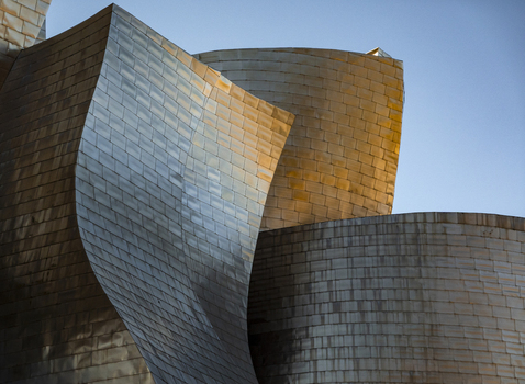 View of the Guggenheim Museum Bilbao featuring curved titanium panels metallic textures and golden reflections under a clear blue sky Bilbao Euskadi Spain. View of the Guggenheim Museum Bilbao featuring curved titanium panels metallic textures and golden reflections under a clear blue sky Bilbao Euskadi Spain.