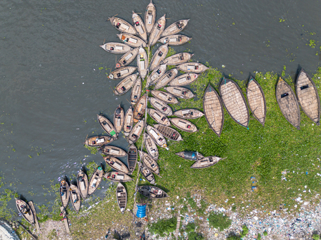 Aerial view of numerous wooden boats clustered along the Buriganga River with green water hyacinths and litter on the shore in Dhaka Dhaka Division Bangladesh.