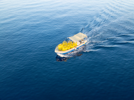 Aerial view of a small boat cuts through the deep blue sea carrying bright yellow cargo under a white canopy Ghajnsielem Gozo Malta. Aerial view of a small boat cuts through the deep blue sea carrying bright yellow cargo under a white canopy Ghajnsielem Gozo Malta.