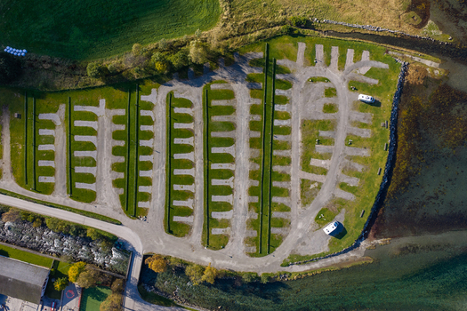 Aerial view of a parking area with gravel spaces and green grass strips located along the shoreline with a few parked vehicles in Geiranger More og Romsdal Norway.
