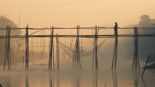 View of a person on a bamboo bridge at sunrise Bangladesh.