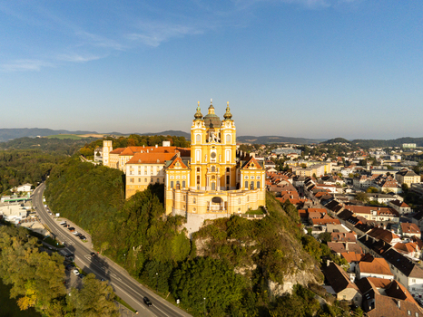 Aerial view of Melk Abbey perched on a rocky outcrop overlooking the town of Melk with historic buildings red rooftops and green hills in Melk Niederosterreich Austria. Aerial view of Melk Abbey perched on a rocky outcrop overlooking the town of Melk with historic buildings red rooftops and green hills in Melk Niederosterreich Austria.
