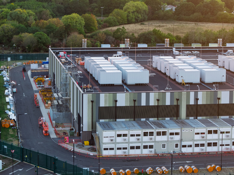 Aerial view of a large data center facility featuring numerous rooftop HVAC units modular office containers and surrounding green landscape in the United Kingdom. Aerial view of a large data center facility featuring numerous rooftop HVAC units modular office containers and surrounding green landscape in the United Kingdom.