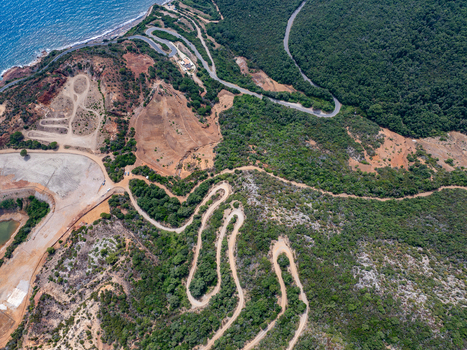 Aerial view of the historic iron mine area near Laghetto delle conche with winding dirt roads rugged reddish terrain and dense vegetation along the coast of Rio Marina Toscana Italy.