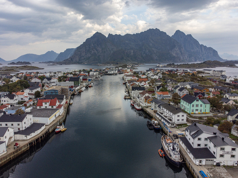Aerial view of the serene waters reflecting the sky nestled between the quaint buildings and the majestic Festvågtind mountains Henningsvær Nordland Norway. Aerial view of the serene waters reflecting the sky nestled between the quaint buildings and the majestic Festvågtind mountains Henningsvær Nordland Norway.