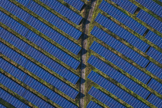 Aerial view of a solar farm with rows of blue photovoltaic panels in a field separated by a path showing the geometric pattern of energy infrastructure in Uckermark Brandenburg Germany.