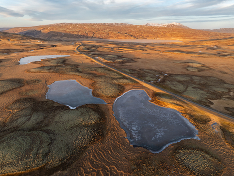 Aerial view of the mossy volcanic landscape with small ponds a winding road and distant mountains under soft golden hour light in Reykjanesbaer Iceland. Aerial view of the mossy volcanic landscape with small ponds a winding road and distant mountains under soft golden hour light in Reykjanesbaer Iceland.