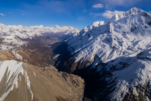 Aerial view of the snow capped Himalayan mountain range with deep valleys rugged peaks and clear blue sky in Nepal.