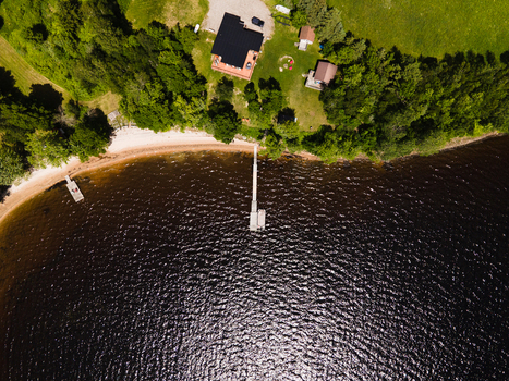 Aerial view of Commanda Lake featuring a wooden dock extending into the dark water a sandy shoreline and a house nestled among lush green trees in Restoule Ontario Canada. Aerial view of Commanda Lake featuring a wooden dock extending into the dark water a sandy shoreline and a house nestled among lush green trees in Restoule Ontario Canada.