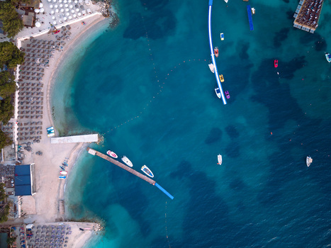 Aerial view of turquoise sea and sandy beach with sunbeds umbrellas and small boats moored at a wooden pier Ksamil Vlore County Albania. Aerial view of turquoise sea and sandy beach with sunbeds umbrellas and small boats moored at a wooden pier Ksamil Vlore County Albania.