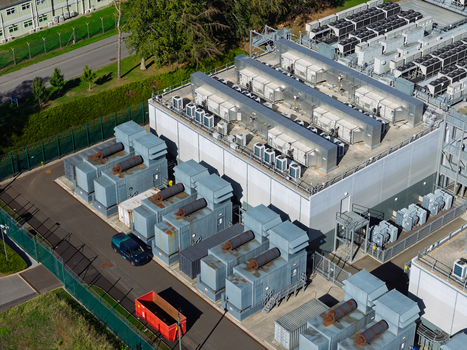 Aerial view of a data center facility featuring industrial cooling units HVAC systems on the rooftop and power infrastructure within a fenced perimeter in the United Kingdom.