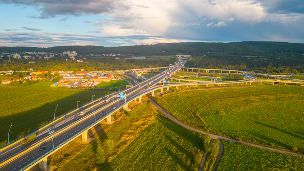 Aerial view of Lahovice Bridge interchange with multi level highway lanes surrounding green fields and suburban buildings under a dramatic sunset sky in Prague Prague Czechia. Aerial view of Lahovice Bridge interchange with multi level highway lanes surrounding green fields and suburban buildings under a dramatic sunset sky in Prague Prague Czechia.