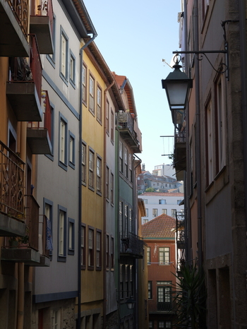 View of a narrow street lined with colorful historic buildings featuring traditional balconies and terracotta roofs in Porto Porto District Portugal. View of a narrow street lined with colorful historic buildings featuring traditional balconies and terracotta roofs in Porto Porto District Portugal.