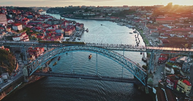 Aerial view of the Dom Luis I Bridge spanning the Douro River featuring a train on the upper deck historic red roofed buildings and golden hour light in Porto Portugal. Aerial view of the Dom Luis I Bridge spanning the Douro River featuring a train on the upper deck historic red roofed buildings and golden hour light in Porto Portugal.