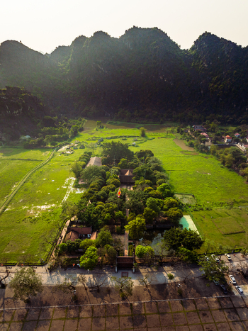 Aerial view of a traditional temple complex nestled among lush green fields and dramatic karst mountains in Vietnam. Aerial view of a traditional temple complex nestled among lush green fields and dramatic karst mountains in Vietnam.