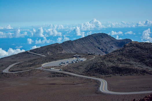 View of the winding road leading to the summit parking area of Haleakala volcano surrounded by rugged volcanic terrain under a clear blue sky in Maui County Hawaii United States.